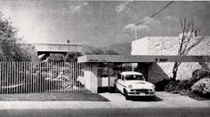 an old car is parked in front of a house with a fence and trees on the other side