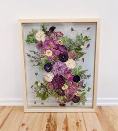 an arrangement of flowers in a wooden frame on the floor next to a white wall