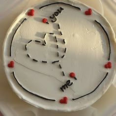 a white cake with writing on it and red hearts around the edges that spell out you're me