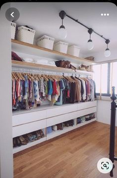 an organized closet with clothes and baskets on the shelves, along with hanging lights above