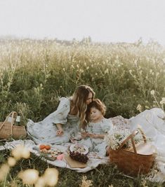 two women sitting on a blanket in the middle of a field with cake and flowers