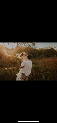 a man carrying a woman in a field with the sun shining through the trees behind him