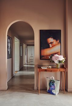 a hallway with a painting and flowers on the table in front of it, along with an archway leading to another room