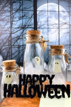 three glass jars with ghost faces and happy halloween written on the front, sitting on a table in front of a full moon