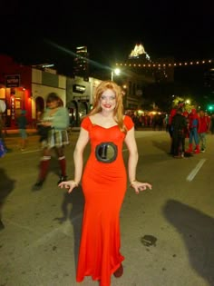 a woman in an orange dress is standing on the street with her hands out and smiling