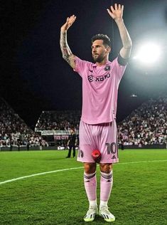 a soccer player is standing on the field waving his hands up to the crowd at night