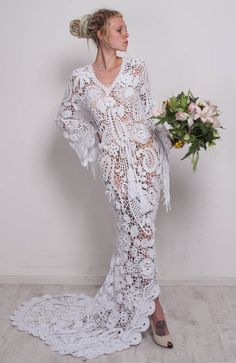 a woman in a white lace dress holding a bouquet and looking off to the side