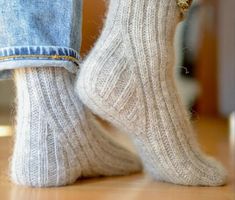 the legs and ankles of a person wearing white socks with blue jeans, standing on a wooden floor