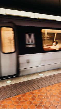 the train is moving fast down the tracks in front of the station platform with its doors open