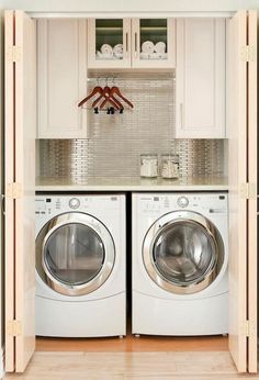 a washer and dryer in a small laundry room with white cabinets, silver tile backsplash