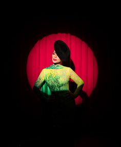 a woman standing in front of a red curtain wearing a black hat and green dress