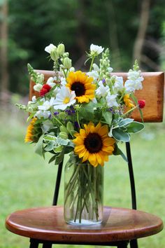 a vase filled with sunflowers and other flowers on top of a wooden chair