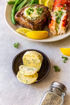 two plates with steak, potatoes and green beans next to lemon wedges on a table