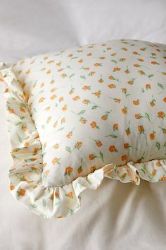 a white pillow with orange flowers and ruffles on it sitting on a bed