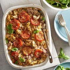 a casserole dish with tomatoes, meat and spinach on the side next to a salad