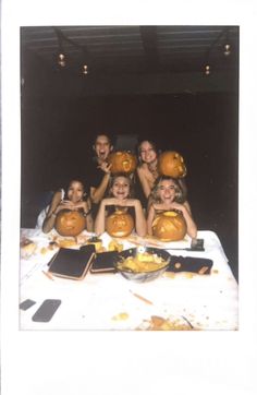 a group of people with pumpkins on their heads sitting at a table in front of them