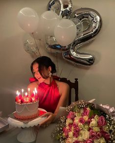 a woman sitting in front of a cake with candles on it and balloons behind her