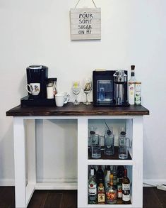 a coffee bar with liquor bottles and cups on it's shelf, next to a wall sign