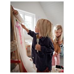 two young children painting on canvases in an art studio, one holding a paintbrush