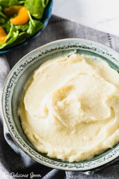 a bowl filled with mashed potatoes on top of a table next to a salad