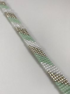 a close up of a bracelet on a white surface with green and silver squares around it