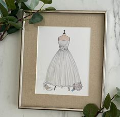 a drawing of a wedding dress is displayed in a frame on a marble countertop