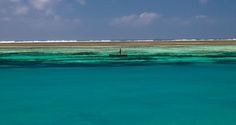 a lone boat floating in the middle of clear blue water with an island in the distance