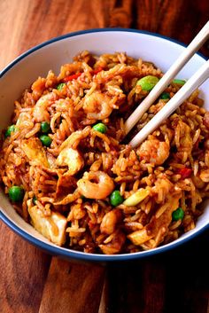 a bowl filled with rice and vegetables on top of a wooden table next to chopsticks