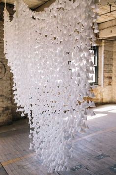 a sculpture made out of white paper hanging from the ceiling in an empty room with brick walls