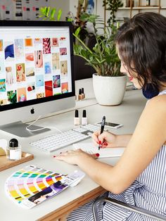 a woman sitting at a desk writing on a piece of paper next to a computer