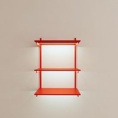 a red shelf sitting on top of a white wall next to a light that is on