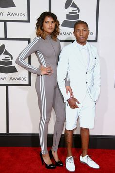 two people standing on a red carpet in front of a wall wearing white and grey outfits