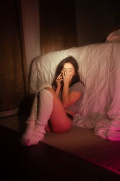 a woman sitting on a bed talking on a cell phone