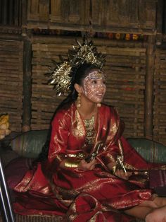 a woman sitting on top of a couch wearing a red and gold dress with her face painted