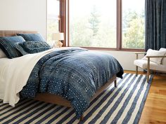 a bedroom with blue and white bedding in front of a large window on a wooden floor