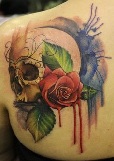 a skull and rose tattoo on the back of a woman's shoulder