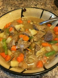 a bowl filled with stew and carrots on top of a granite counter next to a cup of coffee