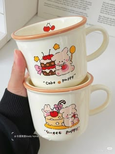 two coffee mugs with cartoon characters on them are held up by someone's hand