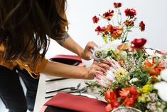 a woman placing flowers on a table with red and white napkins in front of her