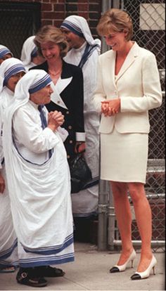 two women dressed in white are talking to each other while others look on from behind the fence