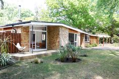 a small brick house sitting in the middle of a lush green yard with lots of trees