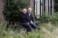 an older couple sitting on a bench in front of a brick building with ivy covered windows