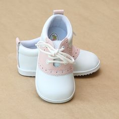 a pair of white and pink baby shoes sitting on top of a brown table next to each other