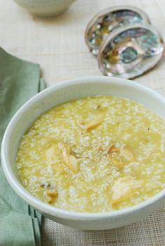 a white bowl filled with soup on top of a table next to silver spoons