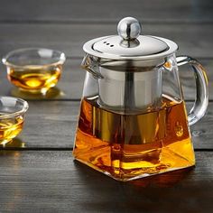 a glass tea pot filled with green tea next to two cups on a wooden table