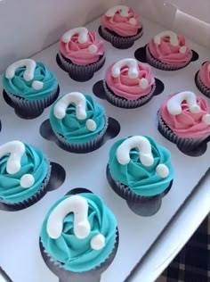 cupcakes with blue, pink and white frosting are arranged in a box