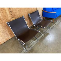 two brown leather chairs sitting next to each other in front of a wooden wall and blue couch