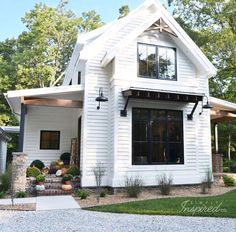 a white house with lots of windows and plants in the front yard, along with gravel driveway