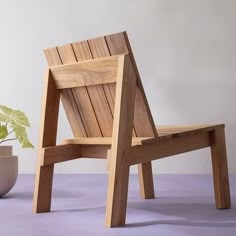 a wooden chair next to a potted plant on a purple surface with white wall in the background