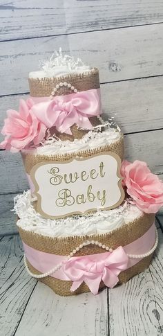 a three tiered baby shower cake with pink flowers on the bottom and burlocks